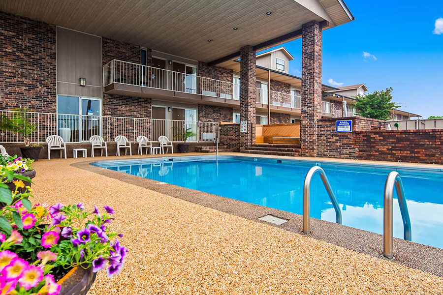 outdoor pool with view of landscaping flowers and patio overhang with chairs underneath at Best Western Sherwood Inn