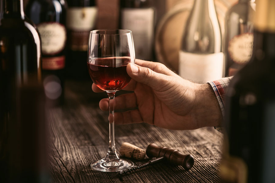 man's hand holding wine glass in a wooden rustic setting